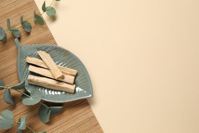 Photo of Palo santo sticks and eucalyptus branches on beige background, flat lay. Space for text