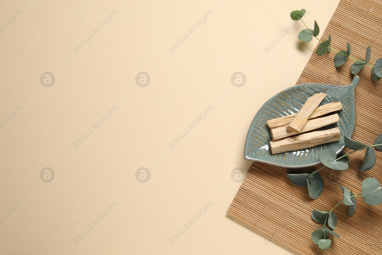 Photo of Palo santo sticks and eucalyptus branches on beige background, flat lay. Space for text