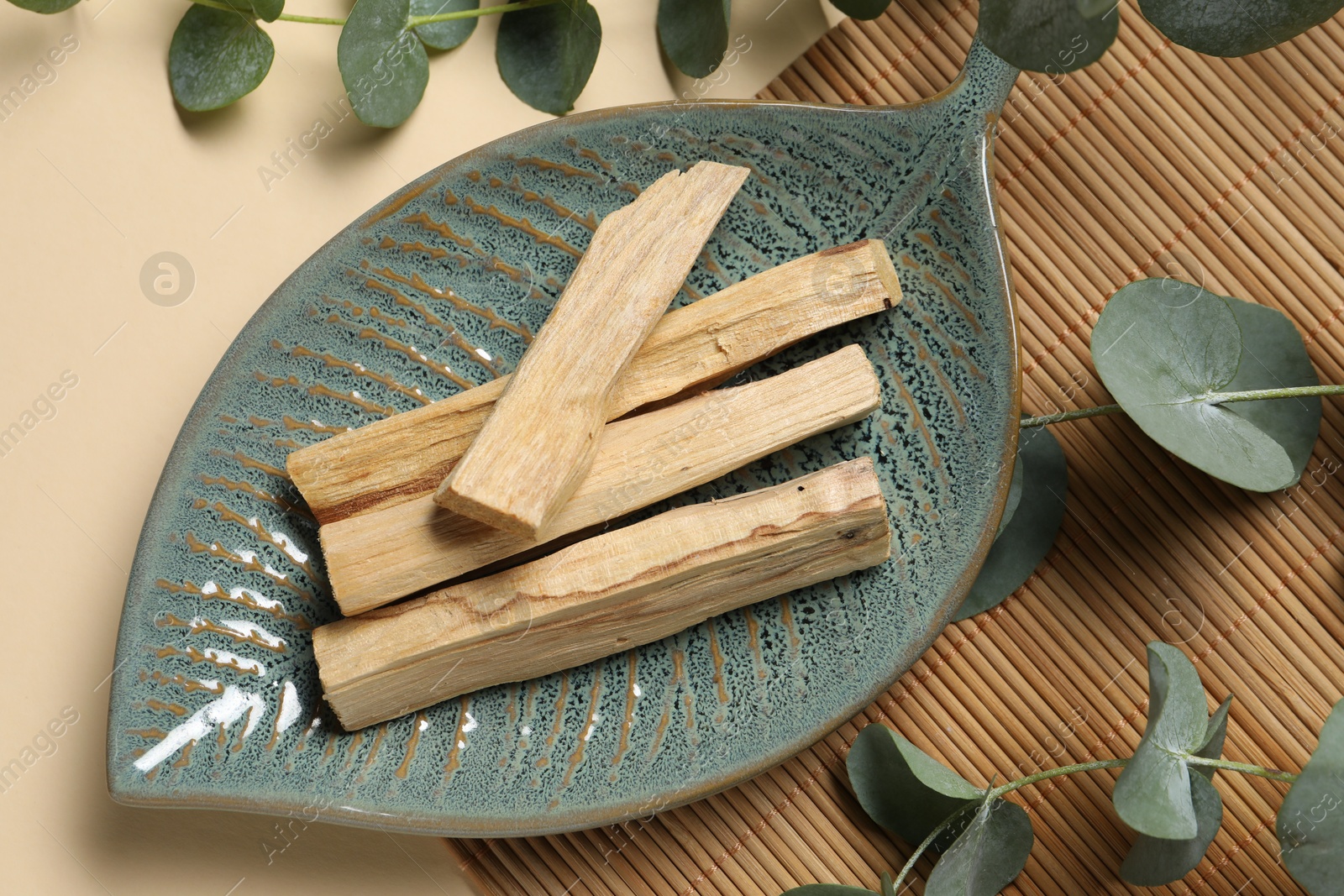 Photo of Palo santo sticks and eucalyptus branches on beige background, flat lay