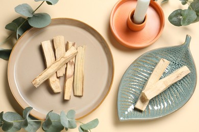 Photo of Palo santo sticks, eucalyptus branches and candle on beige background, flat lay