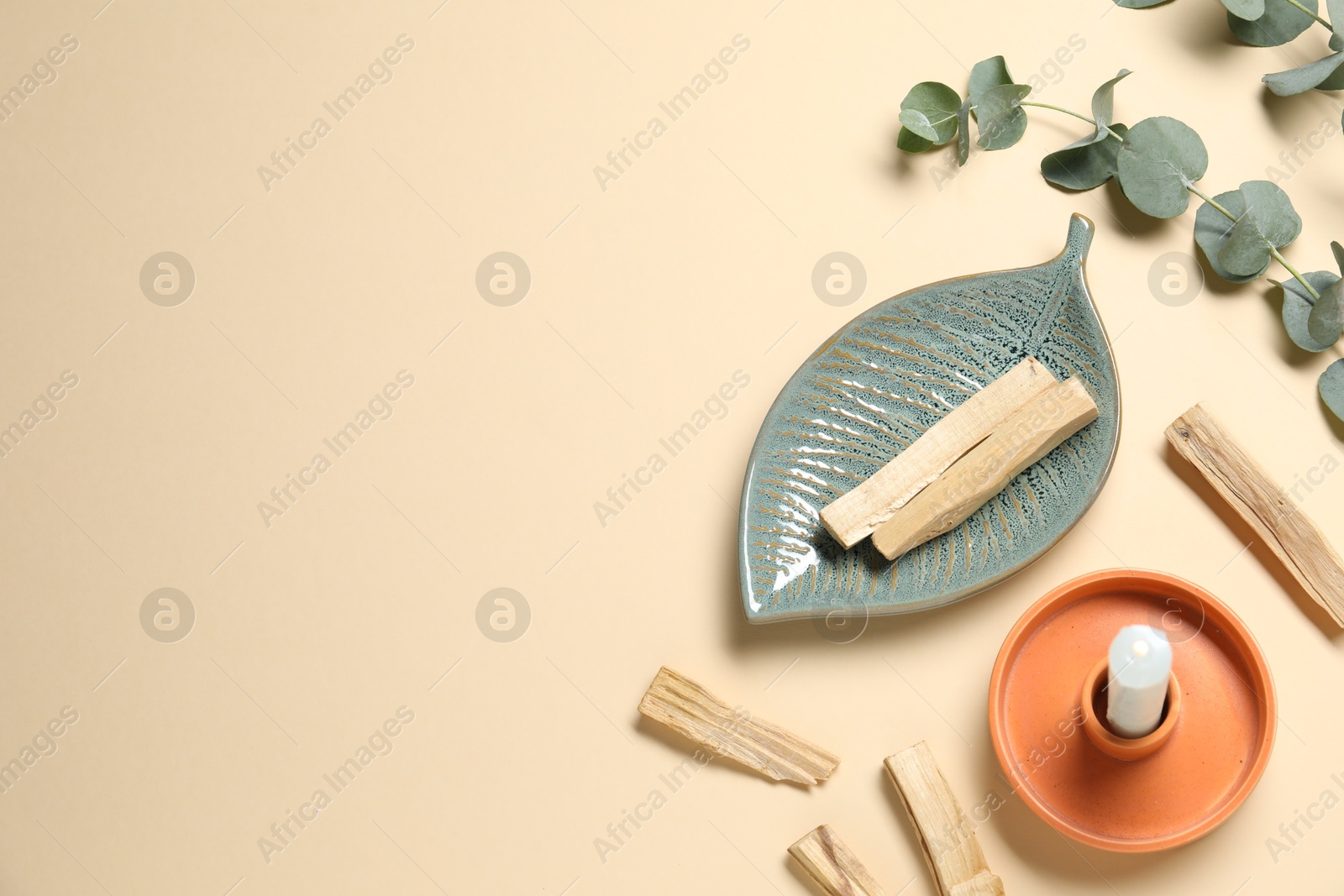 Photo of Palo santo sticks, eucalyptus branches and candle on beige background, flat lay. Space for text