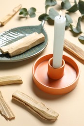 Photo of Palo santo sticks, candle and eucalyptus branches on beige background, closeup