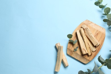 Photo of Palo santo sticks and eucalyptus branches on light blue background, flat lay. Space for text