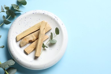 Photo of Palo santo sticks and eucalyptus branches on light blue background, flat lay. Space for text