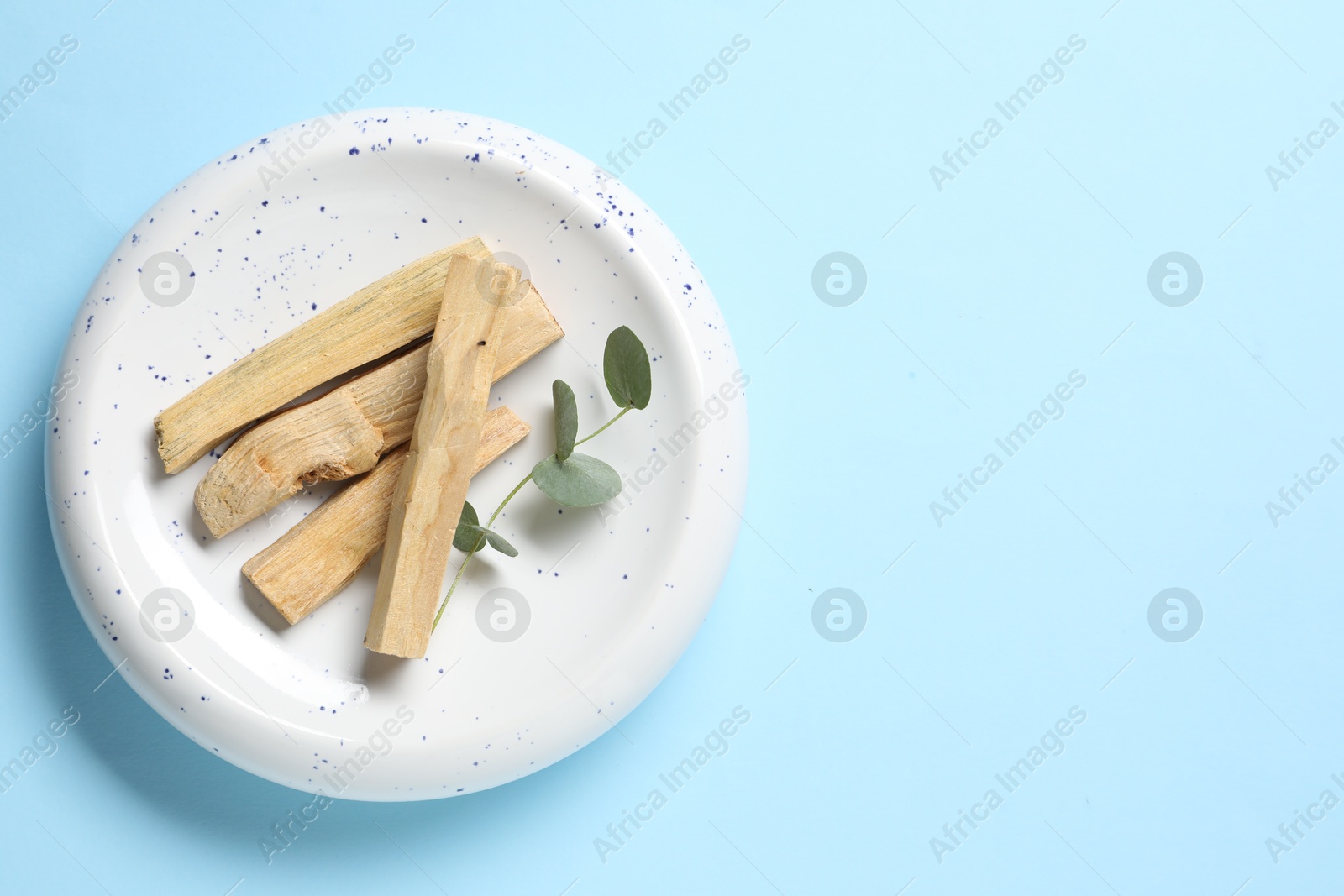 Photo of Palo santo sticks and eucalyptus branch on light blue background, top view. Space for text