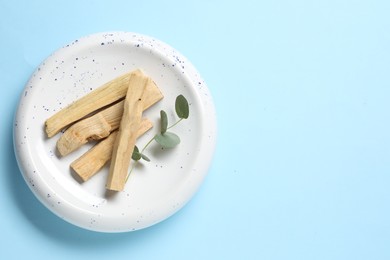 Photo of Palo santo sticks and eucalyptus branch on light blue background, top view. Space for text