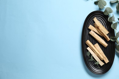 Photo of Palo santo sticks and eucalyptus branches on light blue background, flat lay. Space for text