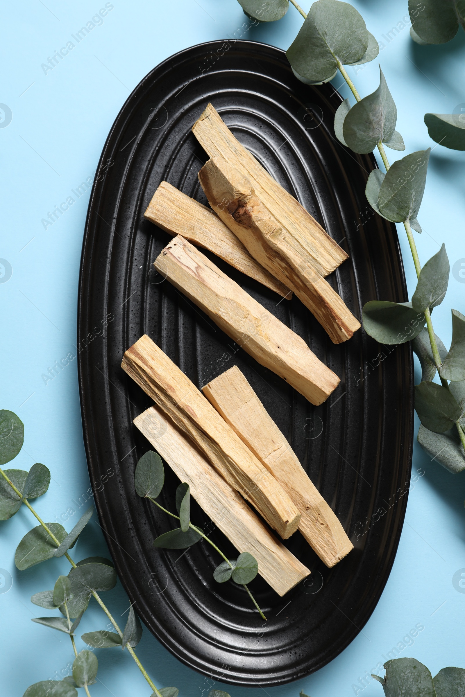 Photo of Palo santo sticks and eucalyptus branches on light blue background, flat lay