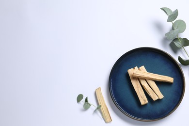 Photo of Palo santo sticks and eucalyptus branches on white background, flat lay. Space for text