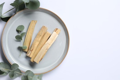 Photo of Palo santo sticks and eucalyptus branches on white background, flat lay. Space for text