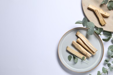 Photo of Palo santo sticks and eucalyptus branches on white background, flat lay. Space for text