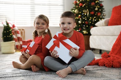 Photo of Happy little children with Christmas gifts on floor at home