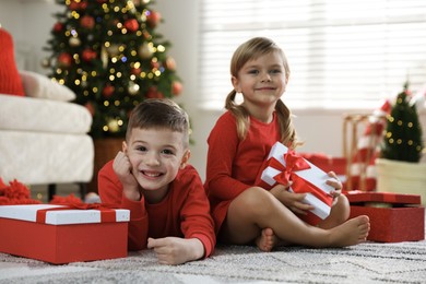 Photo of Happy little children with Christmas gifts on floor at home