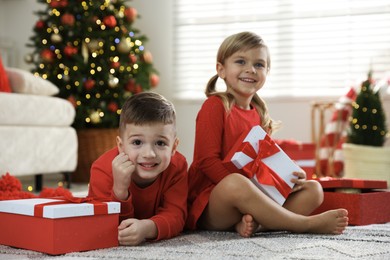 Photo of Happy little children with Christmas gifts on floor at home