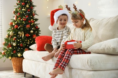 Little children with Christmas gift on sofa at home