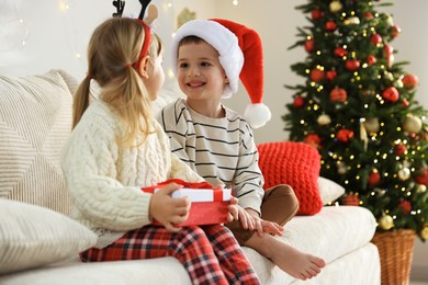 Photo of Little children with Christmas gift on sofa at home