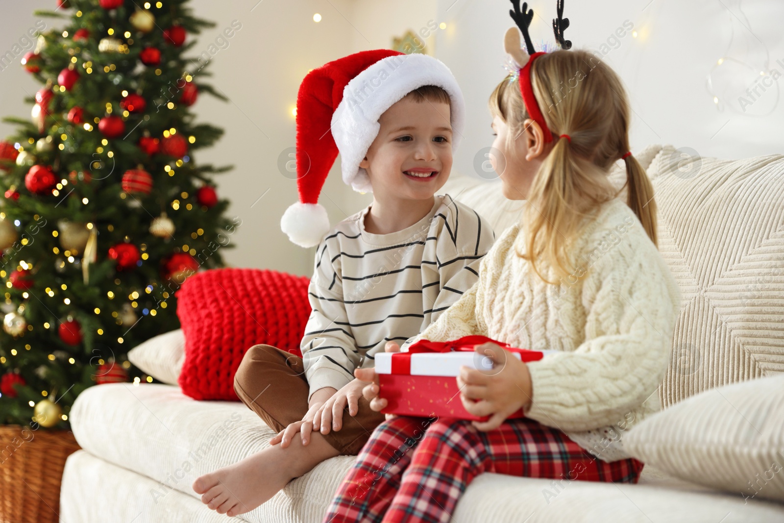 Photo of Little children with Christmas gift on sofa at home