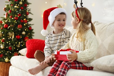 Little children with Christmas gift on sofa at home