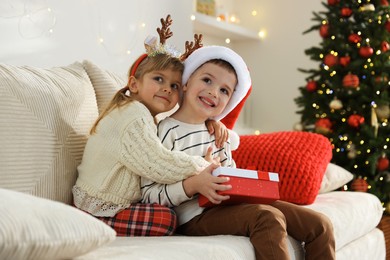 Photo of Happy children with Christmas gift on sofa at home