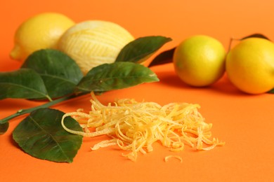 Photo of Lemon zest, fresh fruits and leaves on orange background, closeup