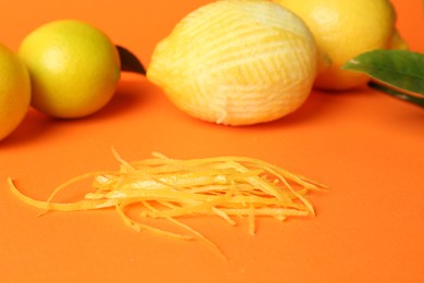 Photo of Lemon zest, fresh fruits and leaves on orange background, closeup