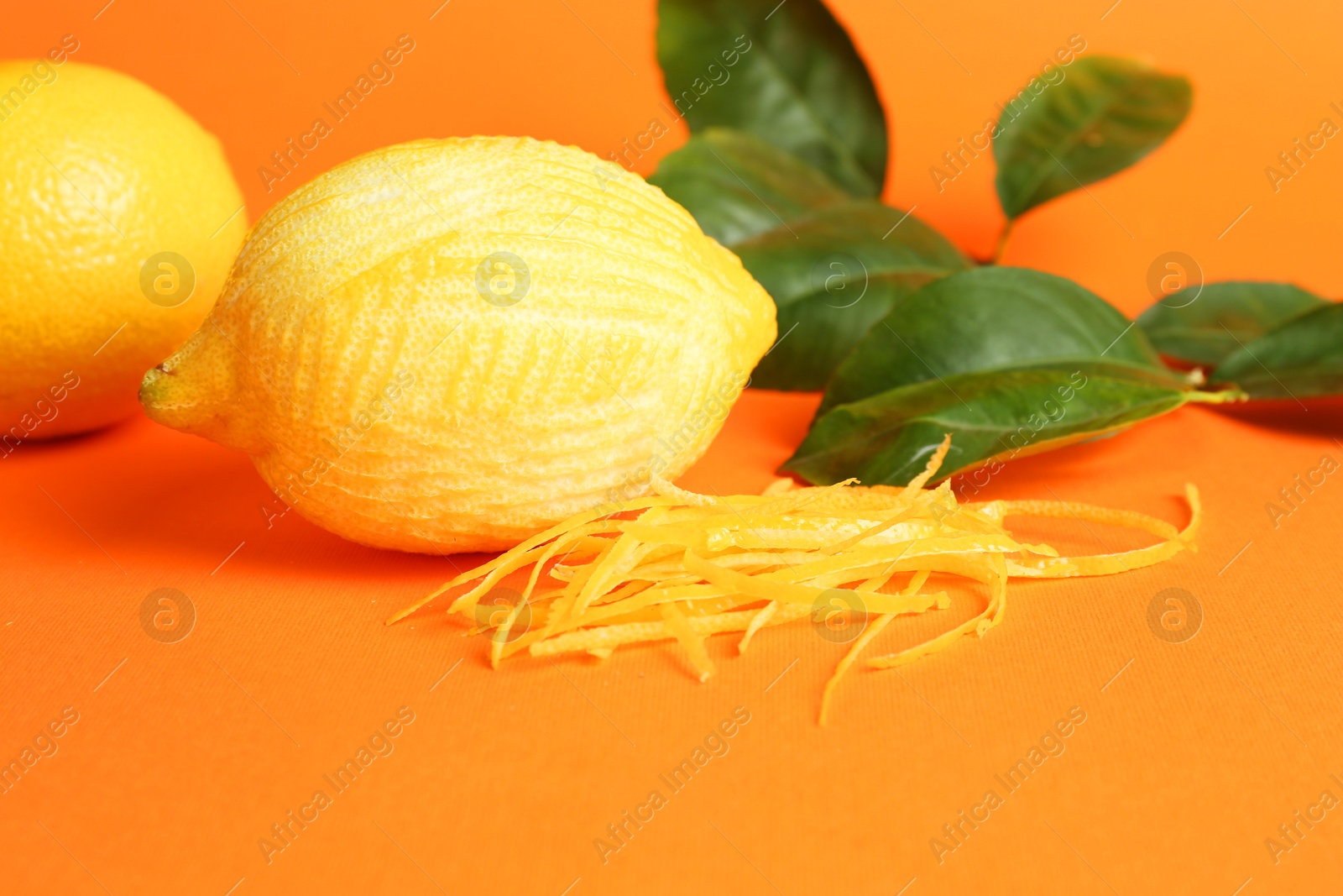 Photo of Lemon zest, fresh fruits and leaves on orange background, closeup