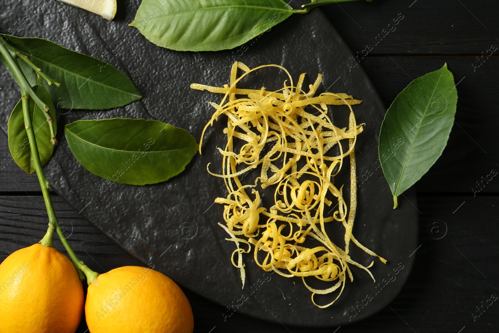 Photo of Lemon zest, fresh fruits and leaves on black wooden table, top view