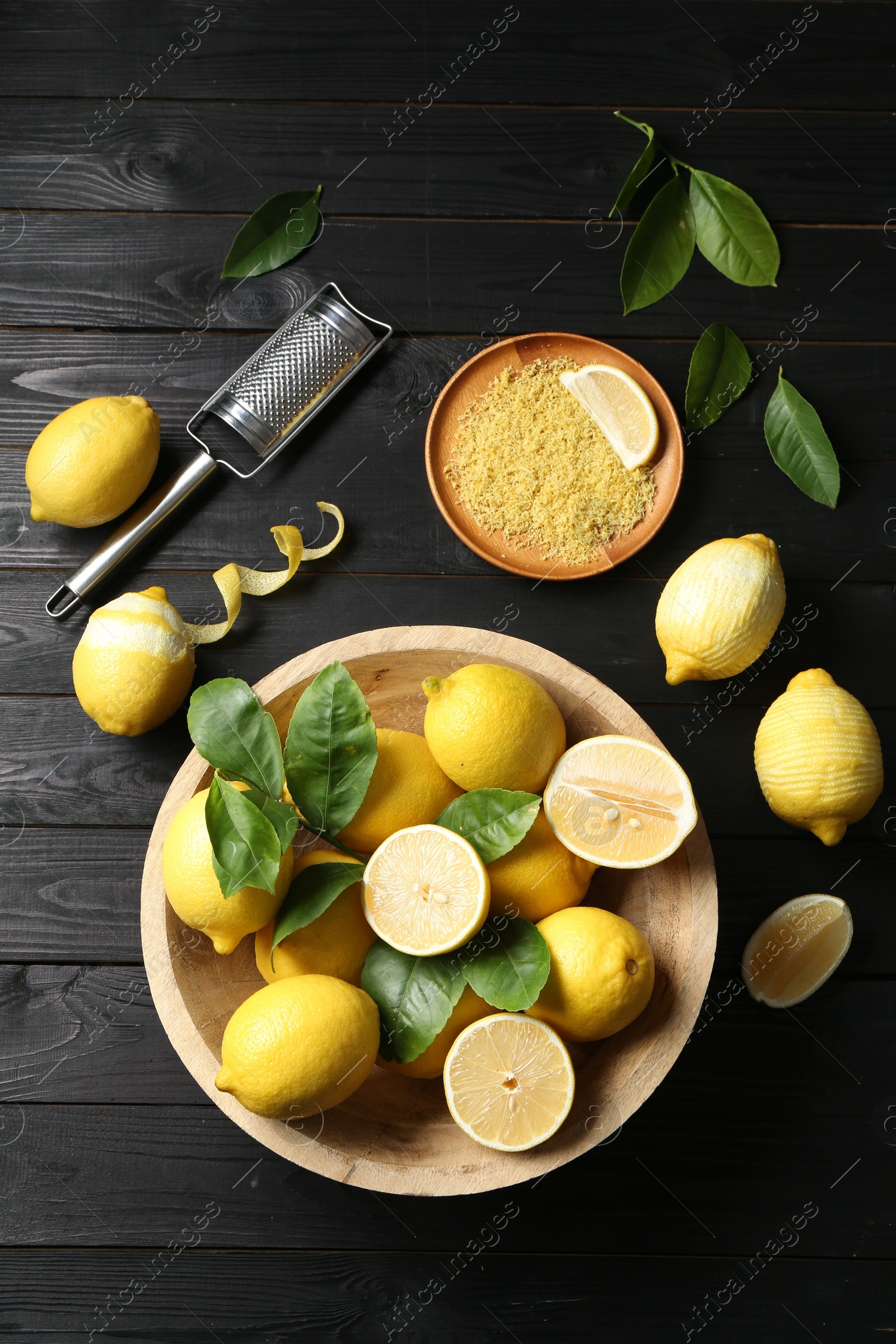 Photo of Lemon zest, grater and fresh fruits on black wooden table, flat lay