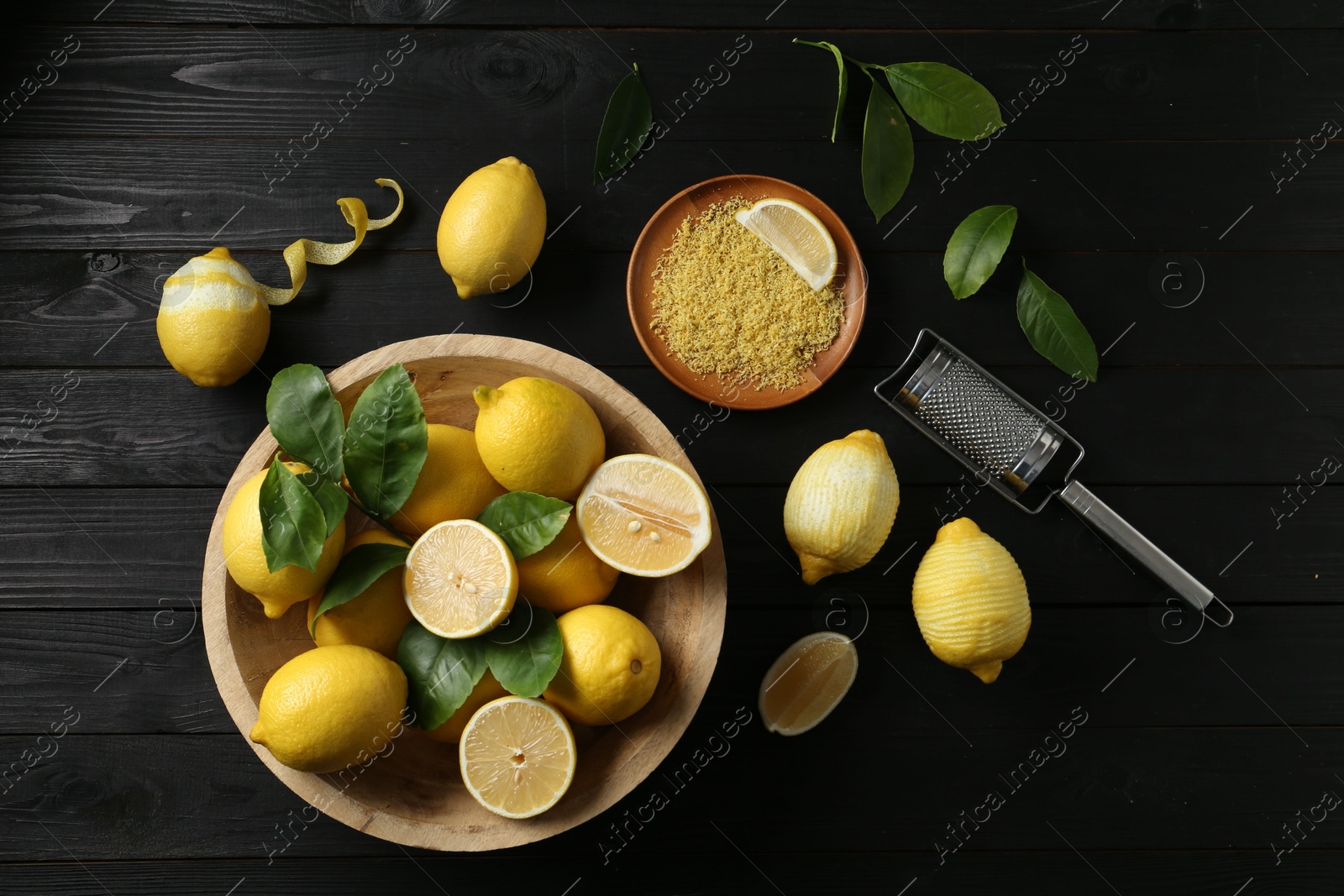 Photo of Lemon zest, grater and fresh fruits on black wooden table, flat lay