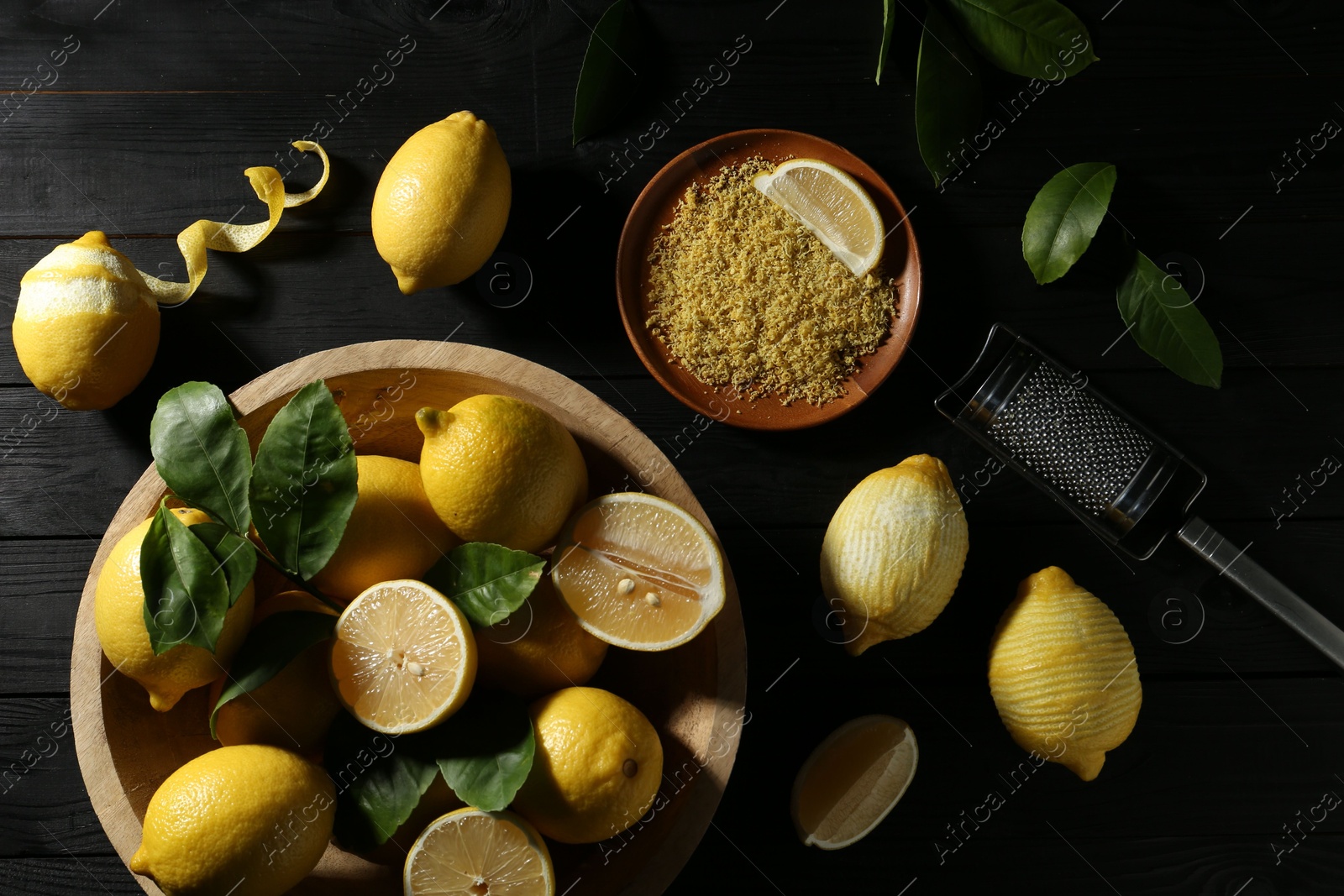 Photo of Lemon zest, grater and fresh fruits on black wooden table, flat lay