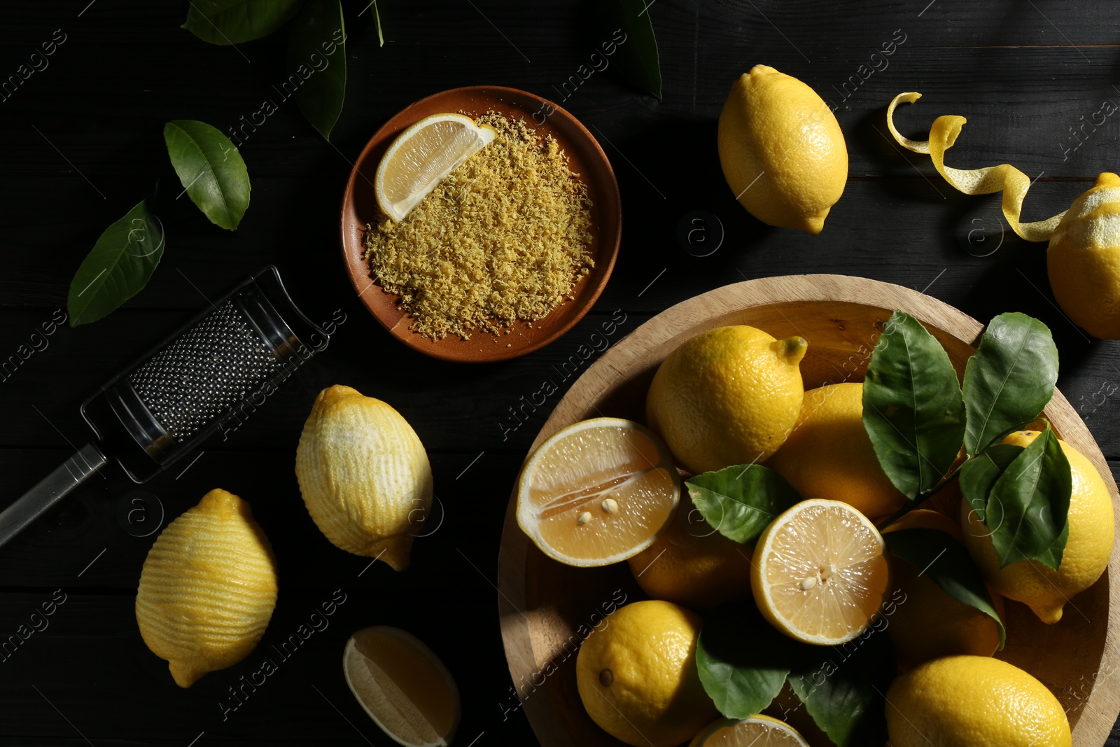 Photo of Lemon zest, grater and fresh fruits on black wooden table, flat lay