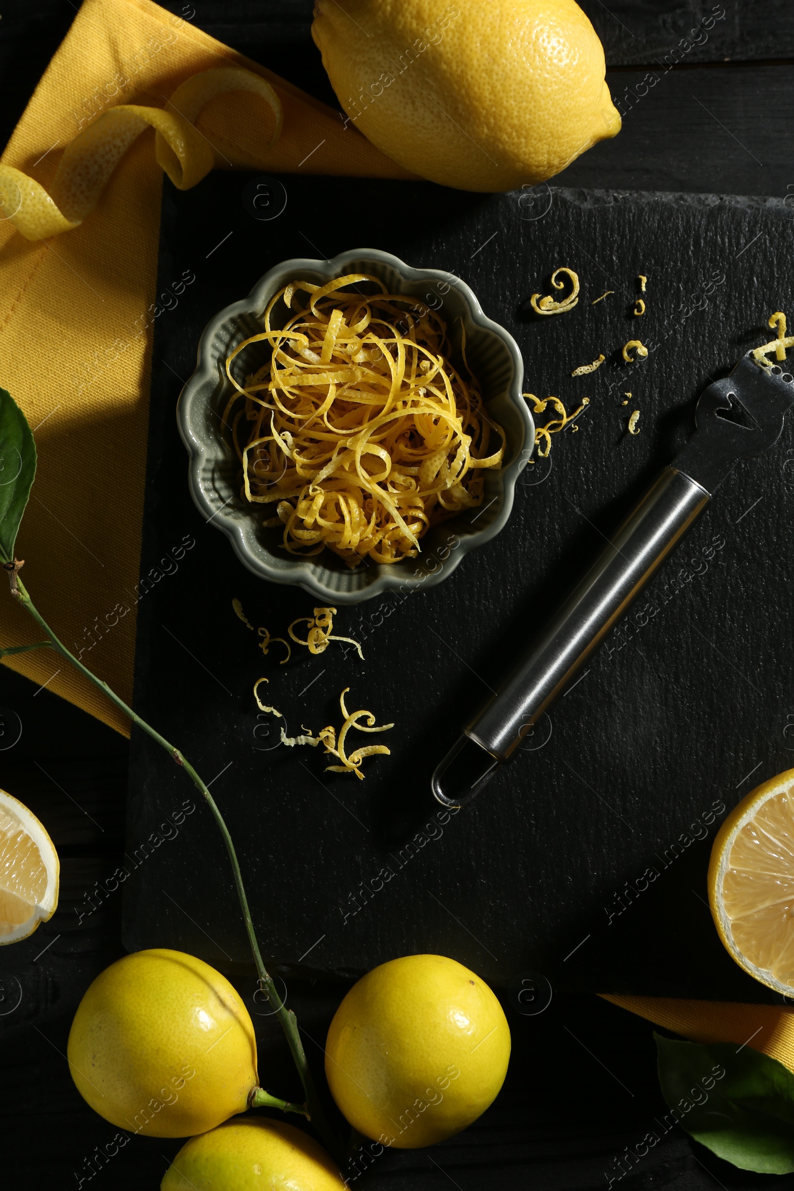 Photo of Lemon zest, fresh fruits and zester tool on black wooden table, flat lay