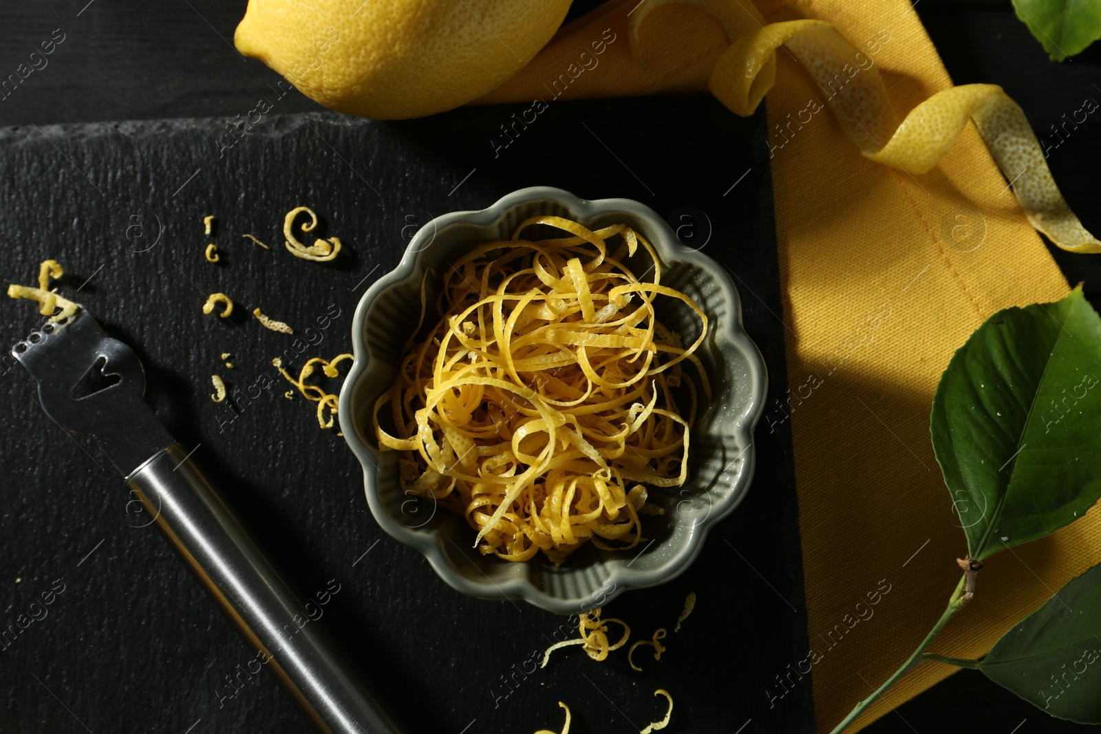 Photo of Lemon zest, fresh fruit and zester tool on black wooden table, flat lay