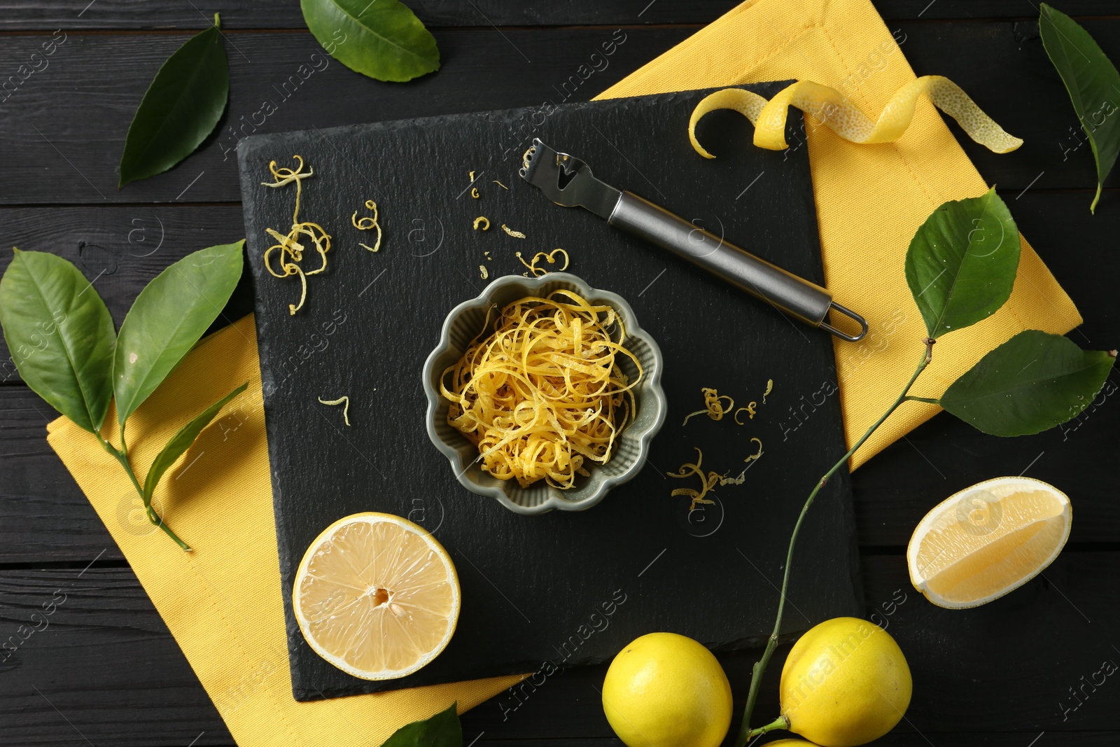 Photo of Lemon zest, fresh fruits and zester tool on black wooden table, flat lay