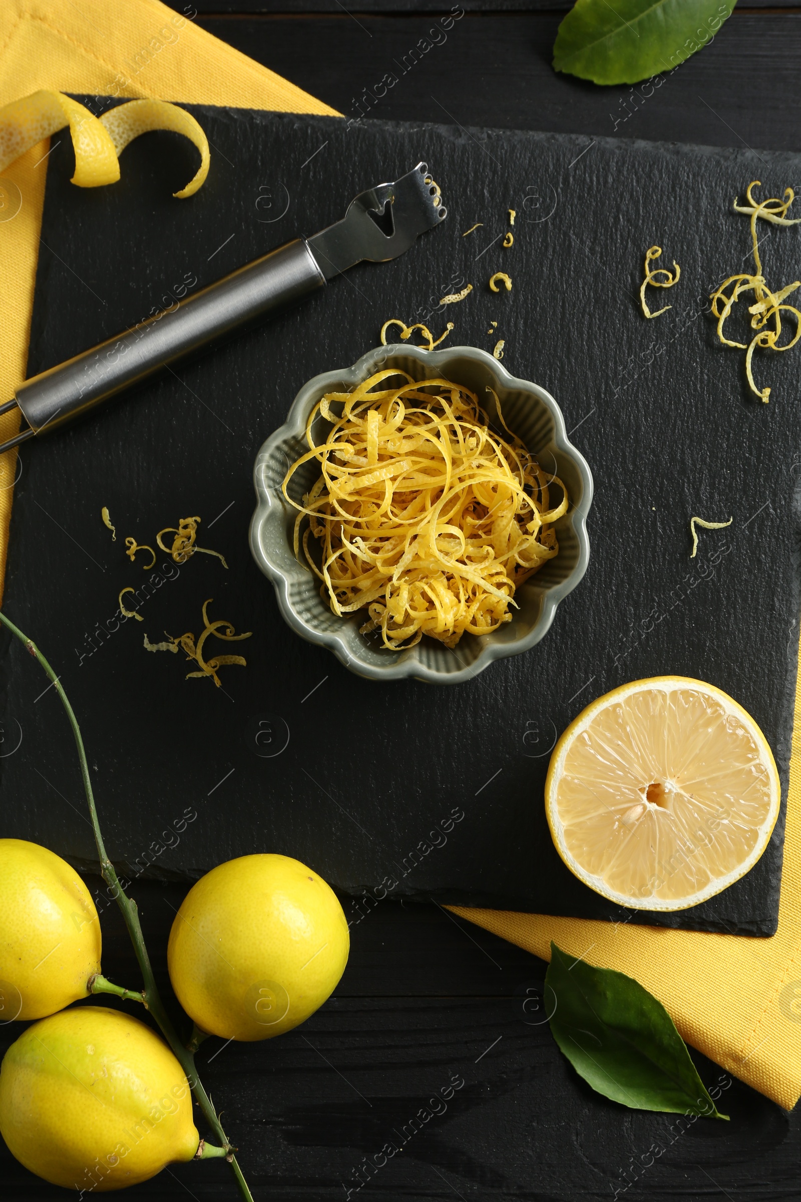 Photo of Lemon zest, fresh fruits and zester tool on black wooden table, flat lay