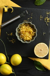 Photo of Lemon zest, fresh fruits and zester tool on black wooden table, flat lay