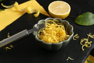 Photo of Lemon zest, zester tool and piece of fresh fruit on black table, closeup