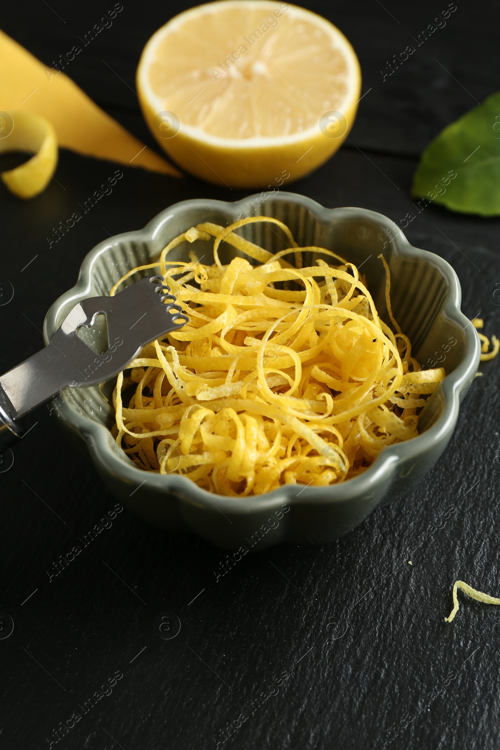 Photo of Lemon zest, zester tool and piece of fresh fruit on black table, closeup