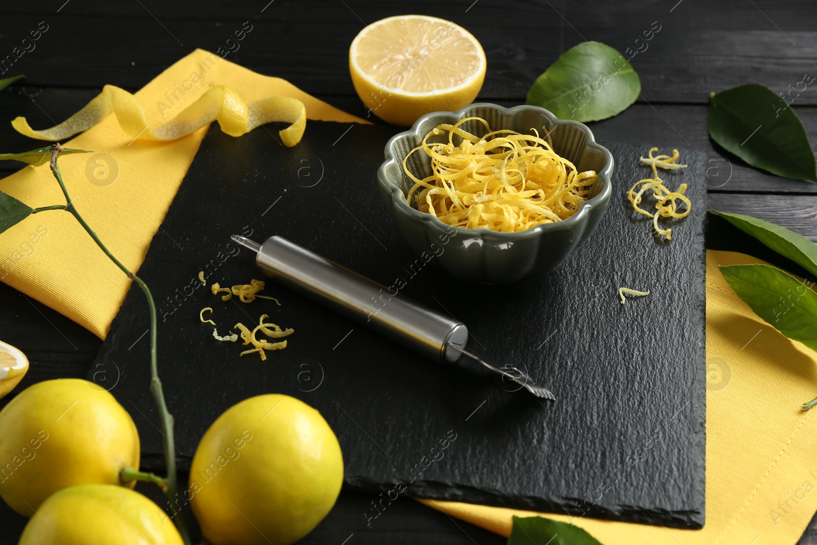 Photo of Lemon zest, zester tool and fresh fruits on black wooden table, closeup