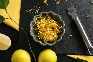 Photo of Lemon zest, zester tool and fresh fruits on black table, flat lay