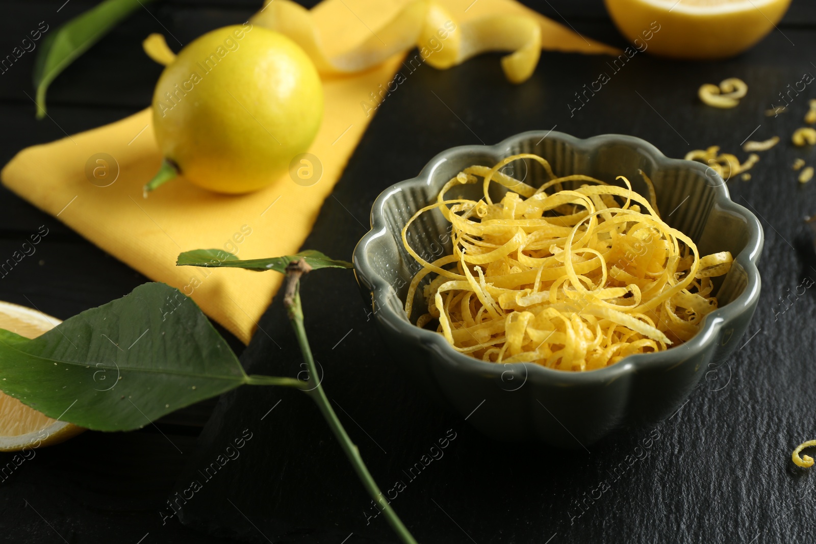 Photo of Lemon zest in bowl and fresh fruits on black table, closeup