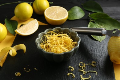 Photo of Lemon zest, zester tool and fresh fruits on black wooden table, closeup