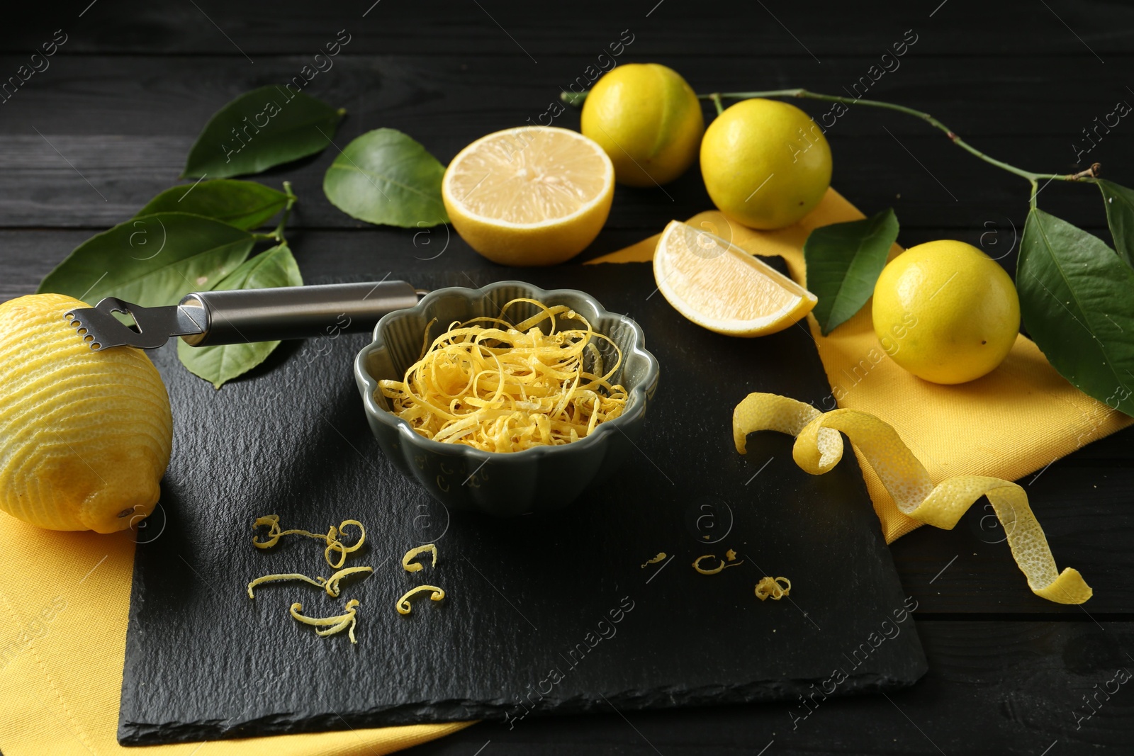 Photo of Lemon zest, zester tool and fresh fruits on black wooden table, closeup