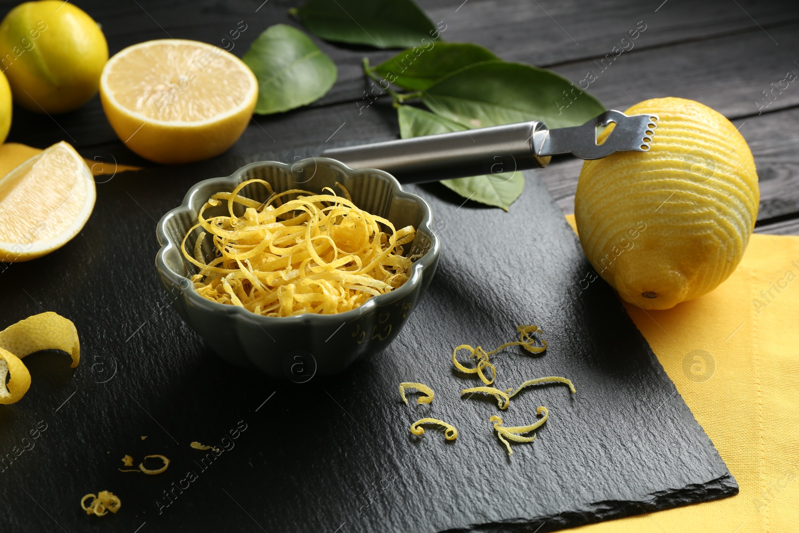 Photo of Lemon zest, zester tool and fresh fruits on black wooden table, closeup