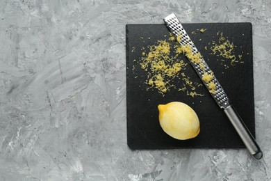 Photo of Lemon zest, grater and fresh fruit on grey textured table, top view. Space for text