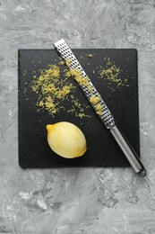 Photo of Lemon zest, grater and fresh fruit on grey textured table, top view