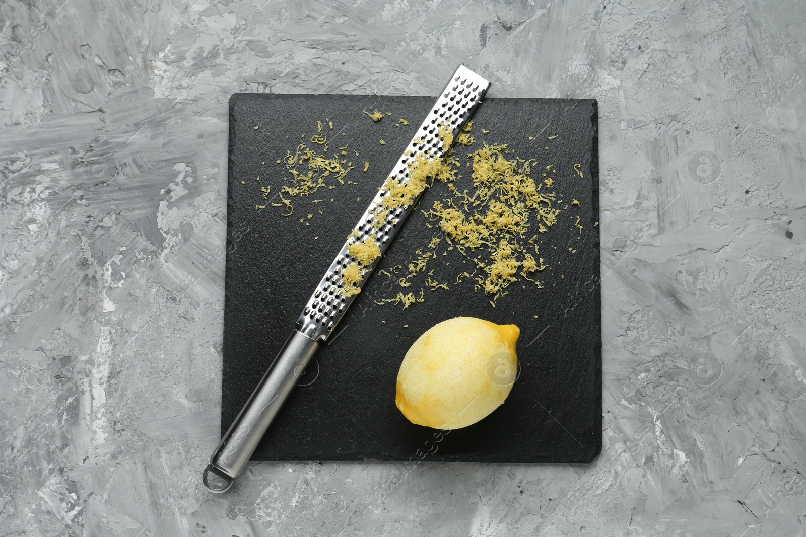 Photo of Lemon zest, grater and fresh fruit on grey textured table, top view