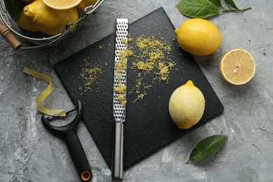 Photo of Lemon zest, tools and fresh fruits on grey textured table, flat lay