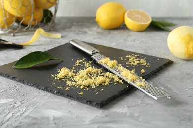 Photo of Lemon zest, grater and fresh fruits on grey textured table, closeup