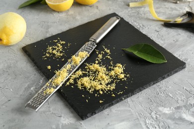 Photo of Lemon zest, grater and fresh fruits on grey textured table, closeup